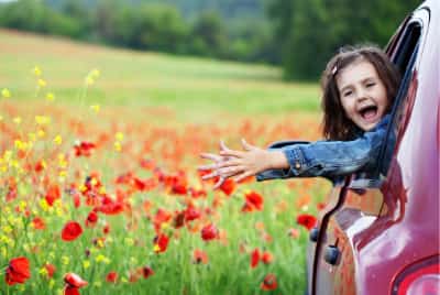 Petite fille souriante à la fenêtre d'une voiture garée dans un champ de coquelicots