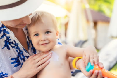 Une femme qui étale de la crème solaire sur le torse d'un jeune enfant