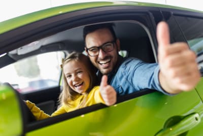 Un homme et une petit fille au volent d'une voiture, souriant avec un pouce levé