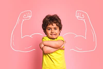 Jeune garçon avec un t-shirt jaune devant des bras musclés dessinés à la craie