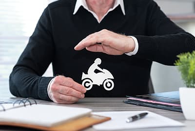 Un homme avec un pull tenant dans sa main droite une moto en papier et la protégeant de la main gauche
