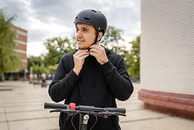 Un jeune homme sur une trottinette électrique en train d'attacher son casque