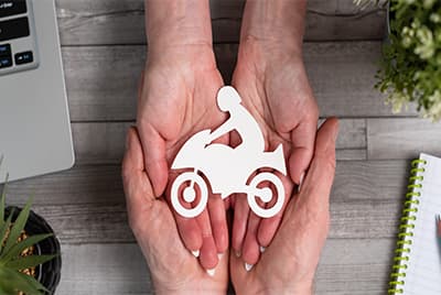 Quatre mains posées l'une sur l'autre sur lesquelles repose une moto en papier blanc