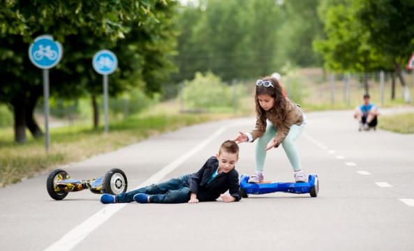 Deux enfants utilisant un hoverboard, l'un est par terre et l'autre vient l'aider