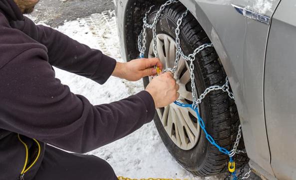 Un homme en train d'installer des chaines sur un pneu