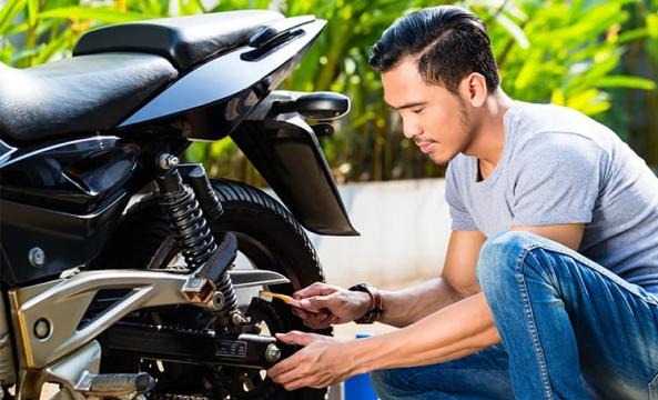 Jeune homme avec un t-shirt gris réparant sa moto