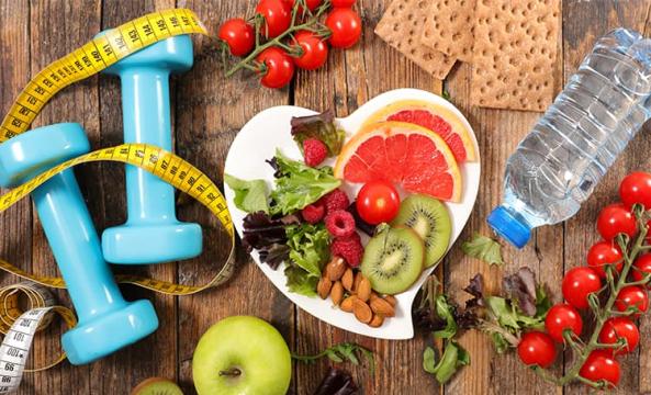 Des petites haltères bleues à côté d'une assiette de fruits et de légumes