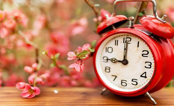 Une horloge rouge posée sur une table à côté de fleurs