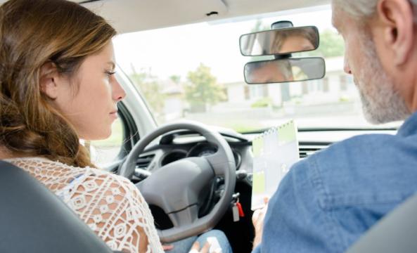 Une jeune fille au volant d'une voiture à côté d'un moniteur d'auto-école