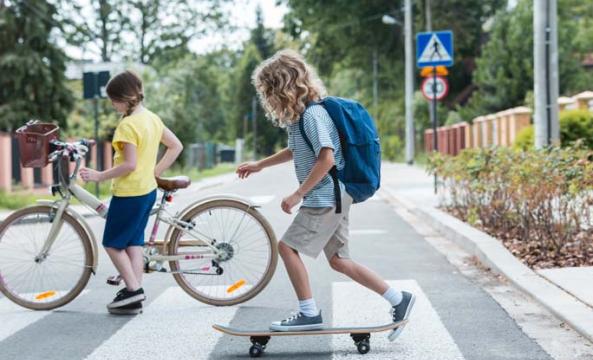 Un enfant sur un skate-board et un enfant sur près d'un vélo en train de traverser la route