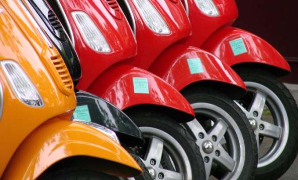 Des scooters rouges et un scooter orange alignés sur la voie
