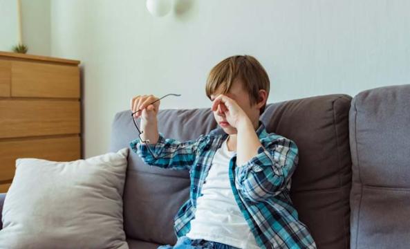 Un jeune garçon tenant ses lunettes d'une main et se frottant les yeux de l'autre main