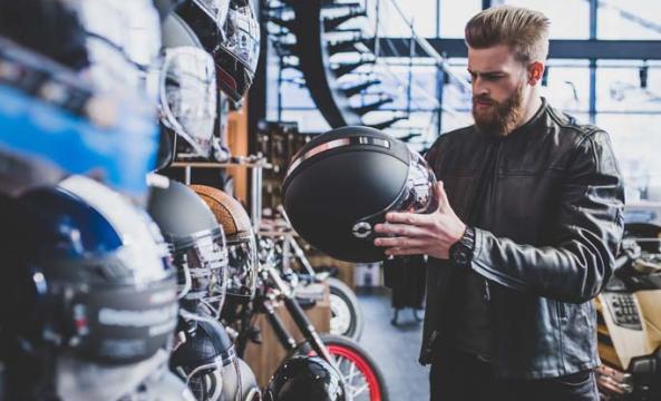 Un homme barbu en train de choisir un casque de scooter dans un magasin spécialisé