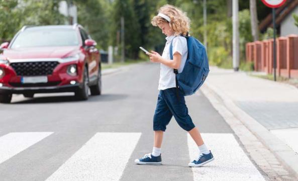 Un jeune enfant avec un sac à dos bleu traversant sur le passage piéton en regardant son téléphone