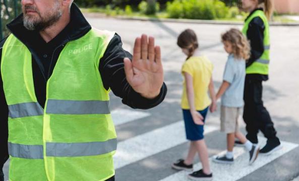 Deux enfants traversant sur le passage piéton encadrés par des agents de circulation