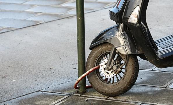 Un scooter attaché à un poteau dans rue à l'aide d'un antivol