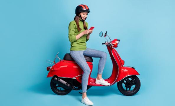 Une jeune femme avec un pull vert assise sur un scooter rouge