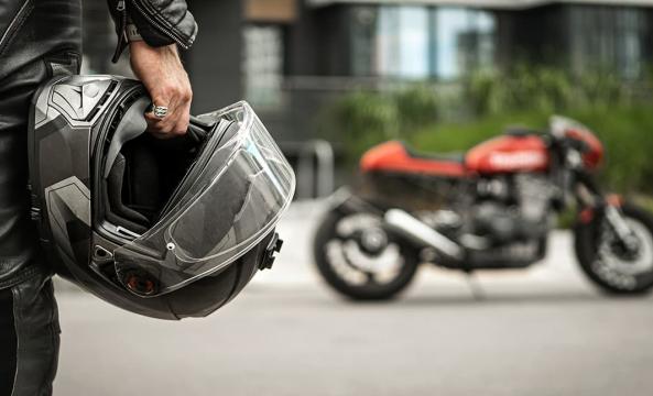 Gros plan sur un motard portant son casque à la main avec une moto rouge en arrière-plan