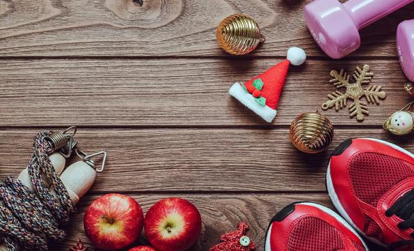 Des haltères roses, une paire de baskets rouges, une corde à sauter, des pommes posés à côté de décorations de Noël