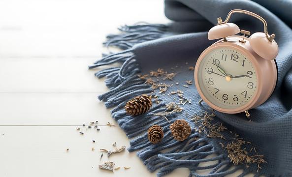 Une horloge rose vintage posée sur une écharpe bleue devant des pommes de pin