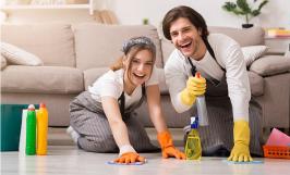 Une jeune femme et un jeune homme souriants nettoyant le sol de leur logement