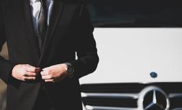 Un homme en costume sombre devant une voiture Mercedes