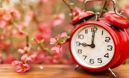 Une horloge rouge posée sur une table à côté de fleurs