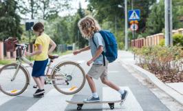 Un enfant sur un skate-board et un enfant sur près d'un vélo en train de traverser la route