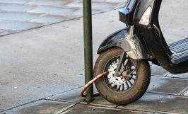 Un scooter attaché à un poteau dans rue à l'aide d'un antivol