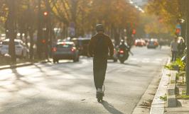 Un jeune homme avec un casque, de dos, circulant sur une trottinette électrique