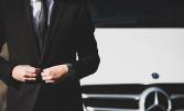 Un homme en costume sombre devant une voiture Mercedes