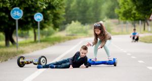 Deux enfants utilisant un hoverboard, l'un est par terre et l'autre vient l'aider