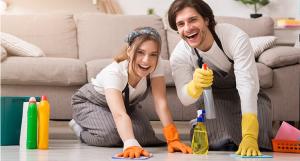 Une jeune femme et un jeune homme souriants nettoyant le sol de leur logement