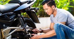 Jeune homme avec un t-shirt gris réparant sa moto