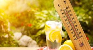Un thermomètre affichant 40°c posé sur un verre rempli d'eau rempli de glaçons et de rondelles de citron
