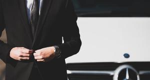 Un homme en costume sombre devant une voiture Mercedes