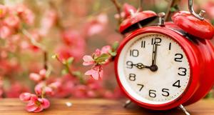 Une horloge rouge posée sur une table à côté de fleurs