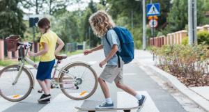 Un enfant sur un skate-board et un enfant sur près d'un vélo en train de traverser la route