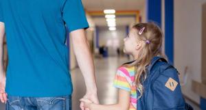 Un papa tenant sa petite fille par la main dans les couloirs d'une école