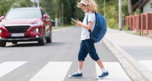 Un jeune enfant avec un sac à dos bleu traversant sur le passage piéton en regardant son téléphone
