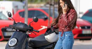 Une jeune fille avec un blouson en cuir bordeaux au téléphone devant son scooter