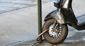 Un scooter attaché à un poteau dans rue à l'aide d'un antivol
