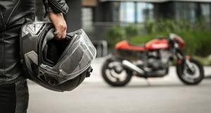 Gros plan sur un motard portant son casque à la main avec une moto rouge en arrière-plan