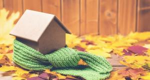 Une écharpe verte entourant une maison miniature en carton sur un fond automnal