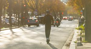 Un jeune homme avec un casque, de dos, circulant sur une trottinette électrique